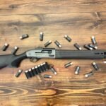 Beretta A300 Ultima Patrol semi-automatic shotgun laid flat on a wooden surface, surrounded by 12-gauge 00 buckshot shells and a side-saddle shell carrier, illustrating a shotgun ammo for home defense setup.