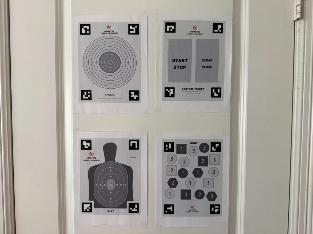 Mantis Laser Academy targets taped to a wall, including bullseye, silhouette, and control targets used for dry fire training with laser systems