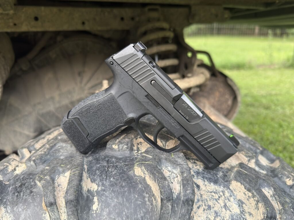 SIG P365 micro-compact 9mm pistol resting on an ATV tire, highlighting the factory sights and slim profile during outdoor field testing.